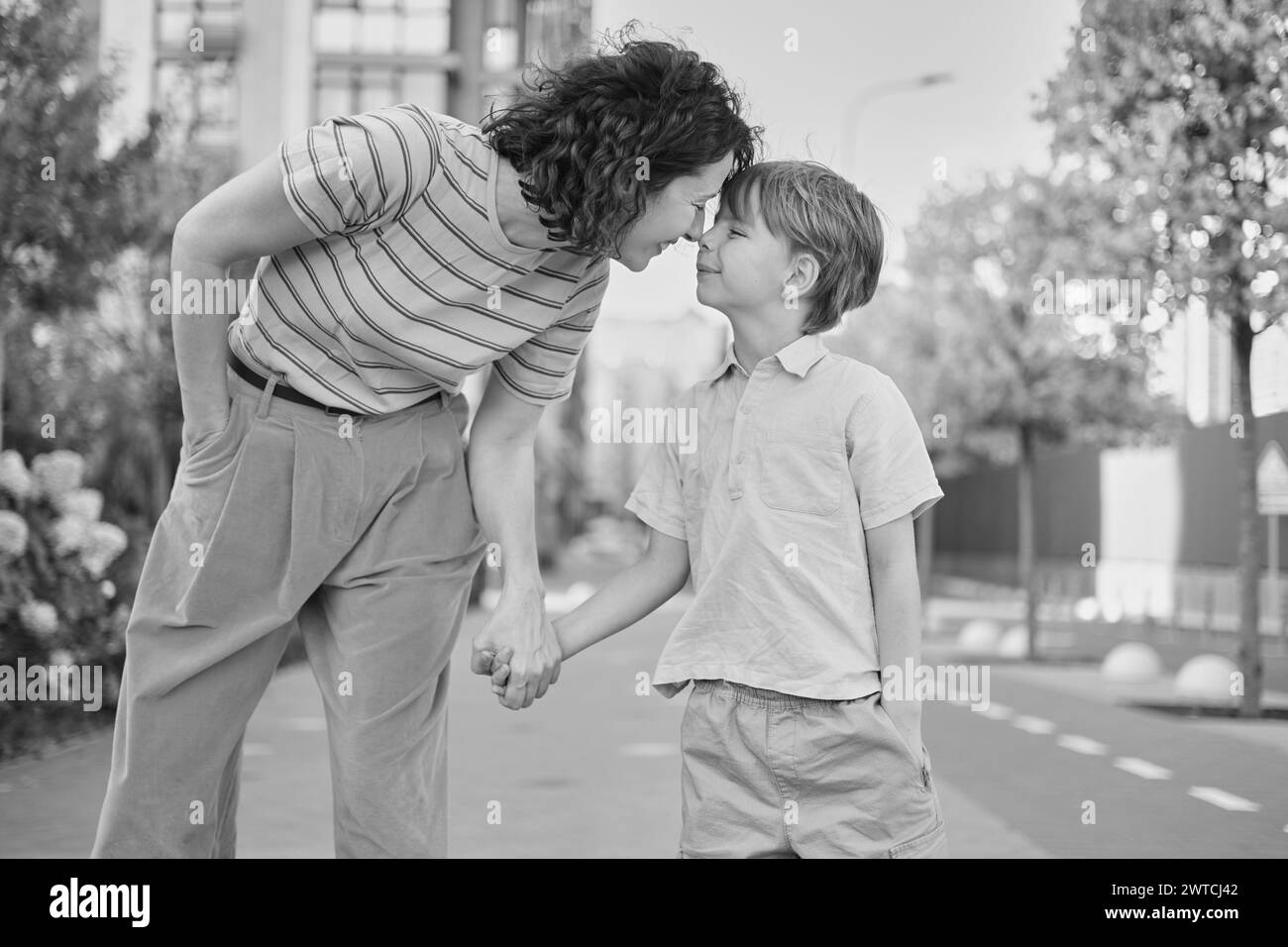 Entzückende Mutter und Sohn lächeln glücklich, Spaß im Hintergrund der Stadt zu haben. Mutterschaft Konzept, Umarmung. Junge 8 Jahre alt mit Mutter in hellen Kleidern, die den Sommertag genießt. Hochwertige Fotos Stockfoto