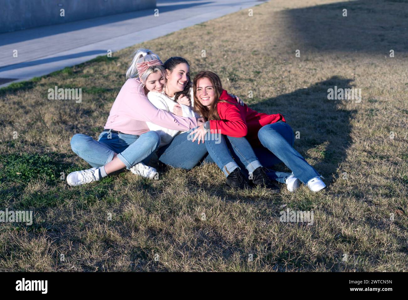 Drei Freunde genießen einen entspannten Moment auf dem Gras, sich im Sonnenlicht zu sonnen, ein Lächeln zu teilen und eine enge Verbindung in lässiger Kleidung zu pflegen Stockfoto