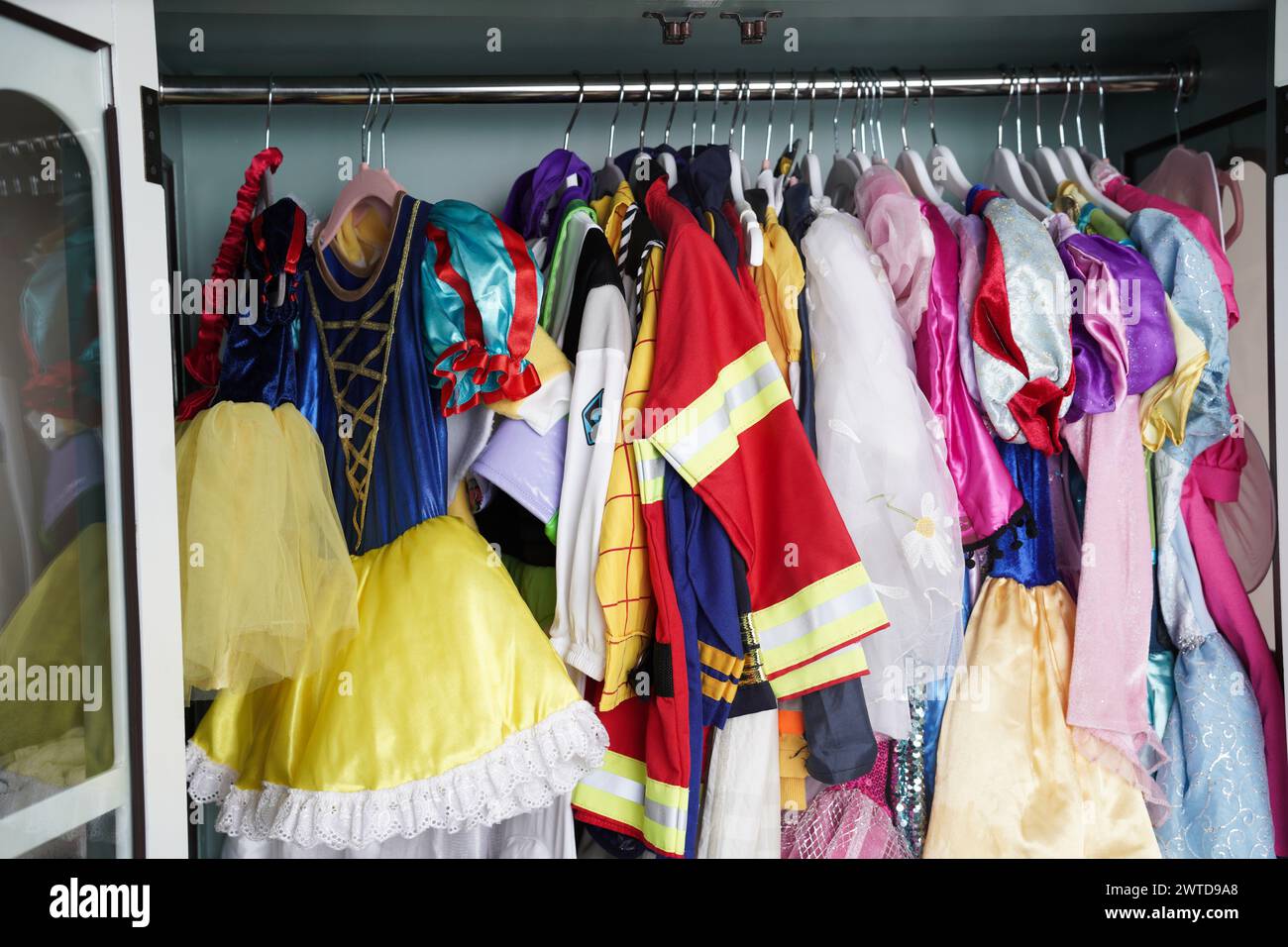 Eine kindliche Garderobe hängt in vertikaler Lagerung. Mädchen- und Jungenkleidung sowie Halloween-Kostüme hängen ordentlich in einem Schrank. Stockfoto