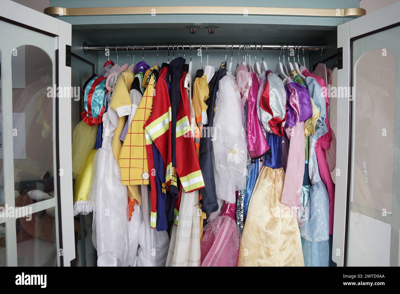 Eine kindliche Garderobe hängt in vertikaler Lagerung. Mädchen- und Jungenkleidung sowie Halloween-Kostüme hängen ordentlich in einem Schrank. Stockfoto