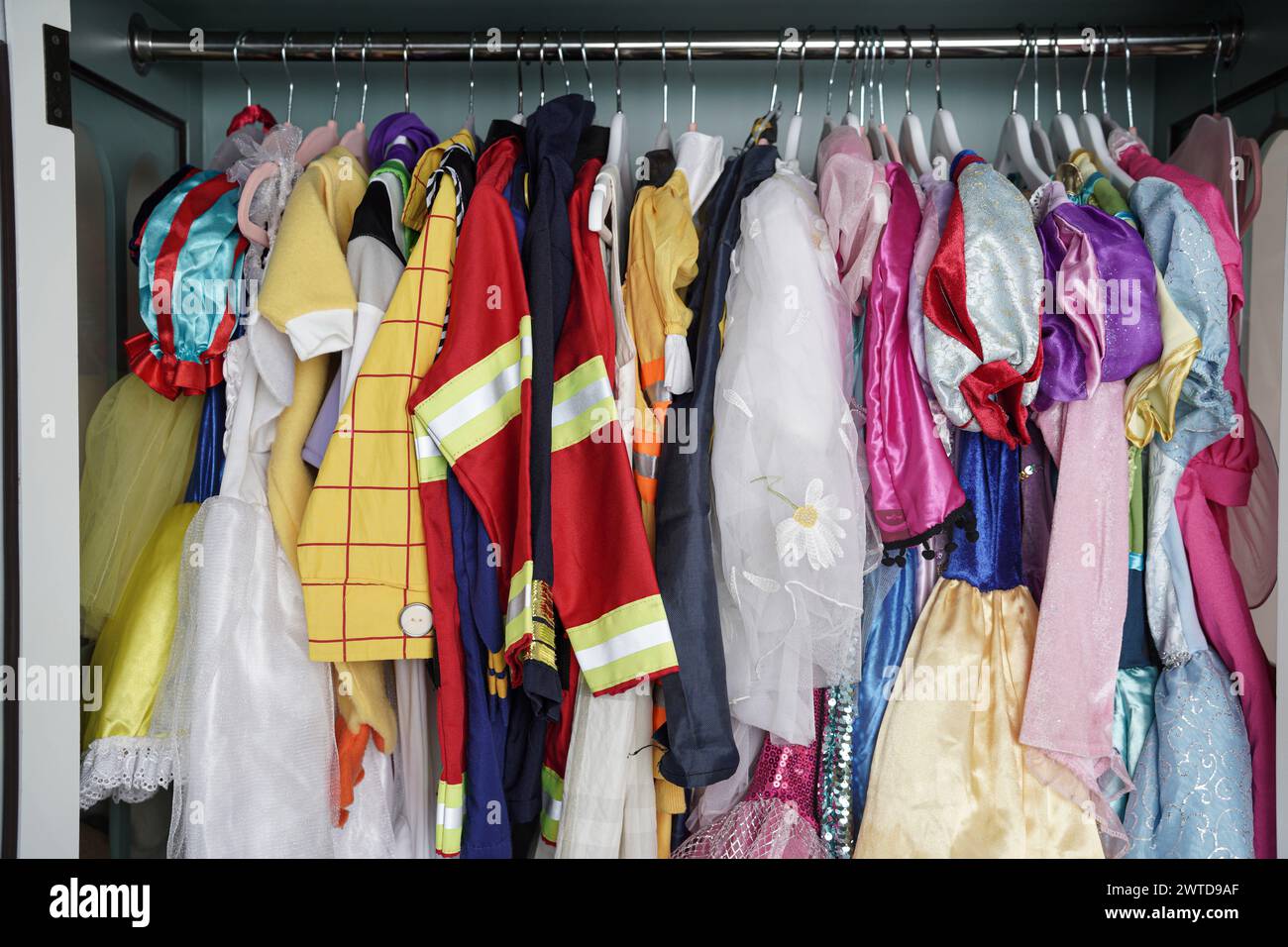 Eine kindliche Garderobe hängt in vertikaler Lagerung. Mädchen- und Jungenkleidung sowie Halloween-Kostüme hängen ordentlich in einem Schrank. Stockfoto