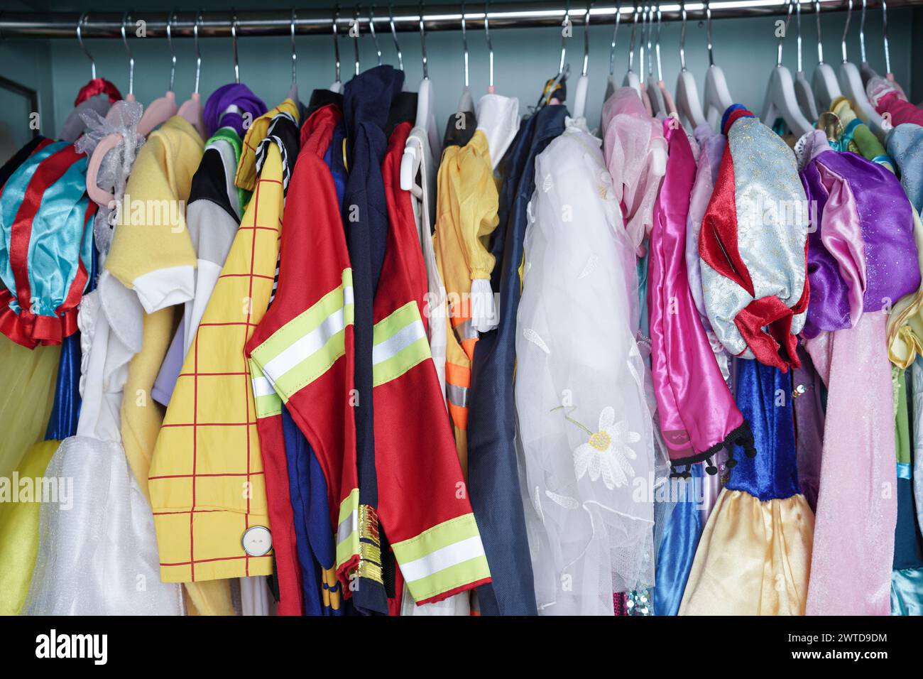 Eine kindliche Garderobe hängt in vertikaler Lagerung. Mädchen- und Jungenkleidung sowie Halloween-Kostüme hängen ordentlich in einem Schrank. Stockfoto