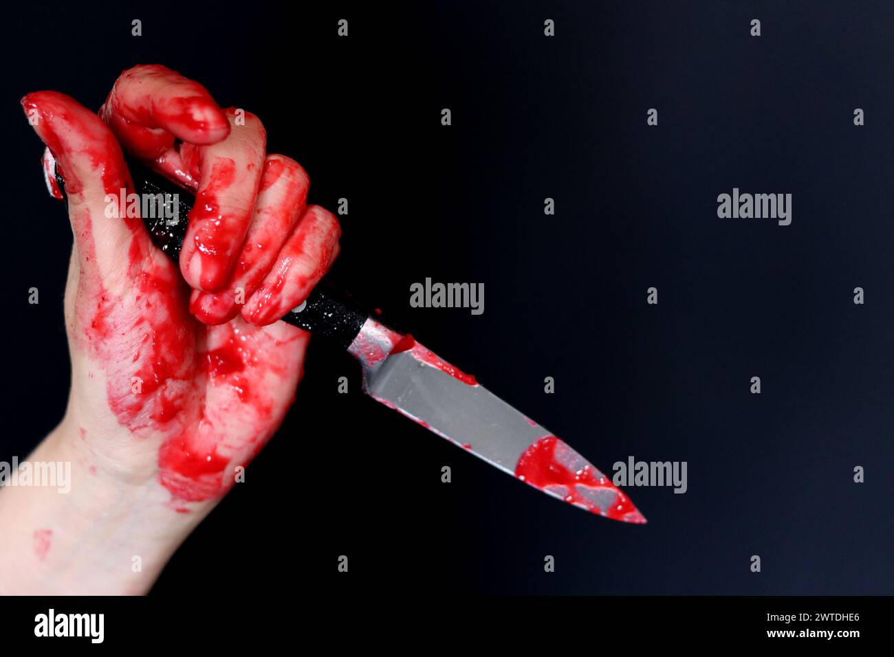 Blutige Hand, die ein Messer mit Blut auf schwarzem Hintergrund hält. Mordkonzept häuslicher Gewaltmissbrauch Stockfoto