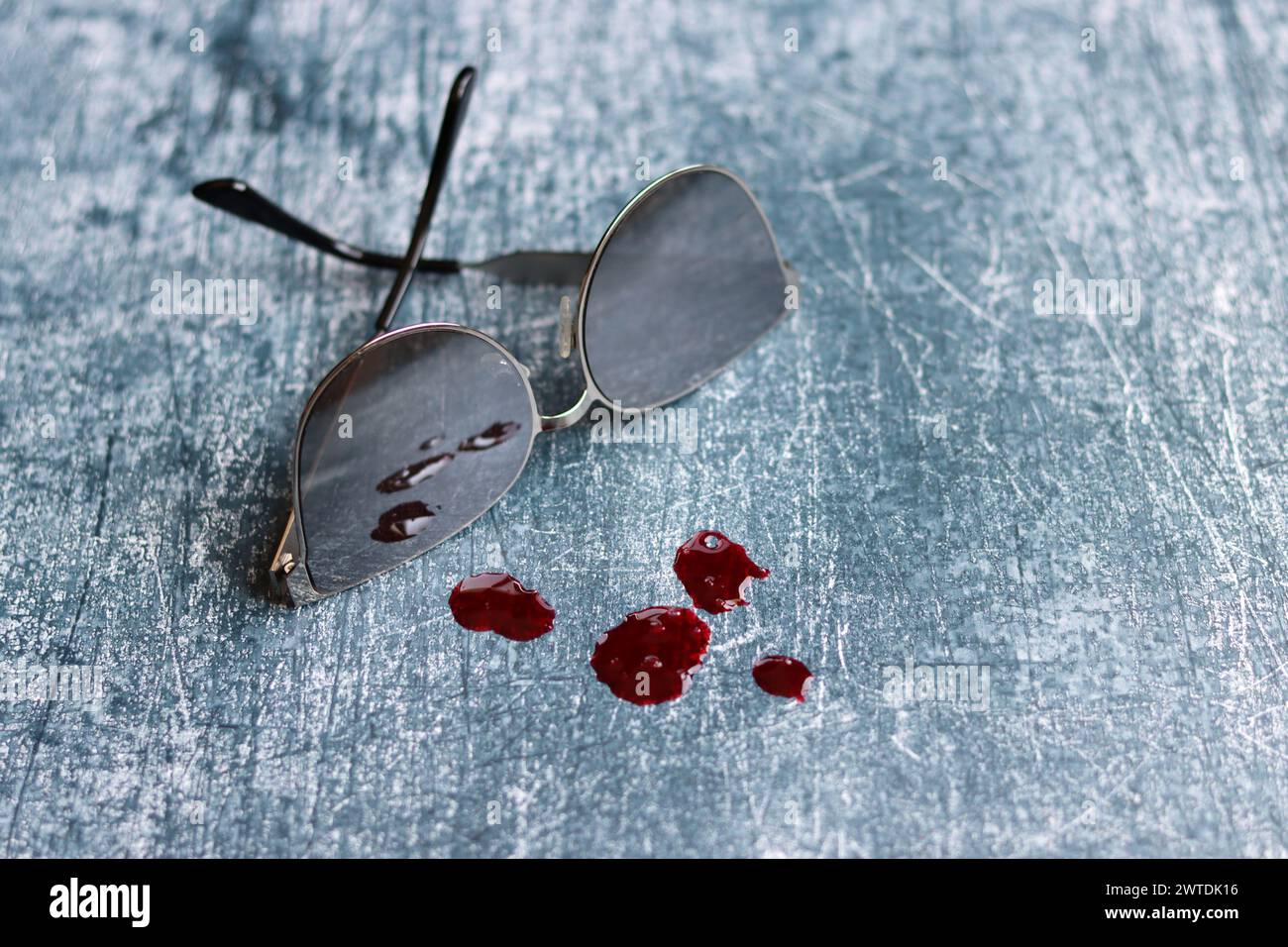 Sonnenbrille und Bluttropfen auf grauem, strukturiertem Hintergrund mit Kopierraum. Tatortkonzept. Stockfoto