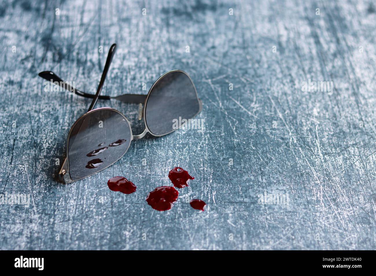 Sonnenbrille und Bluttropfen auf grauem, strukturiertem Hintergrund mit Kopierraum. Tatortkonzept. Stockfoto