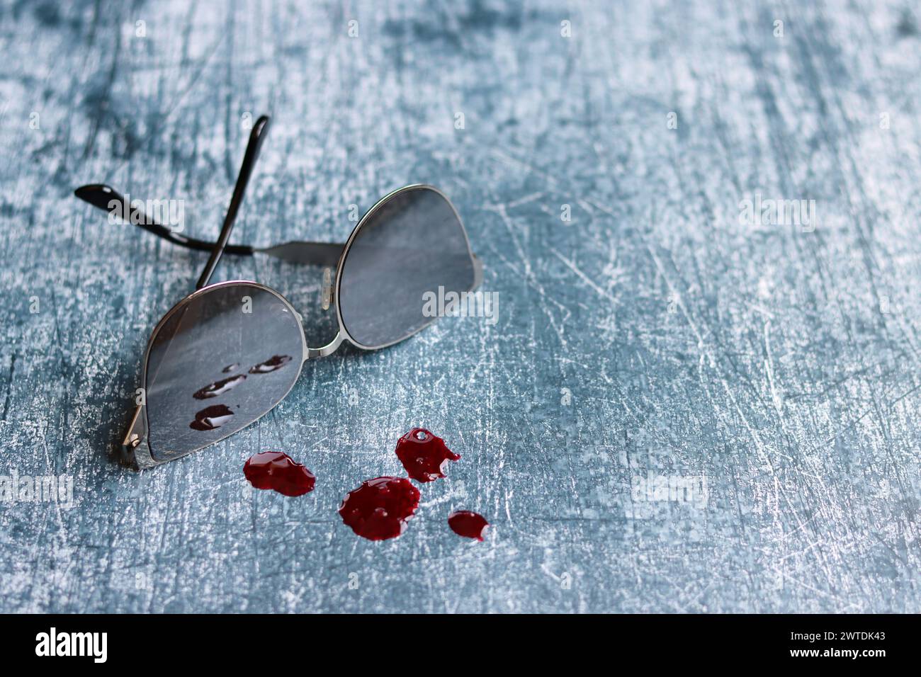 Sonnenbrille und Bluttropfen auf grauem, strukturiertem Hintergrund mit Kopierraum. Tatortkonzept. Stockfoto