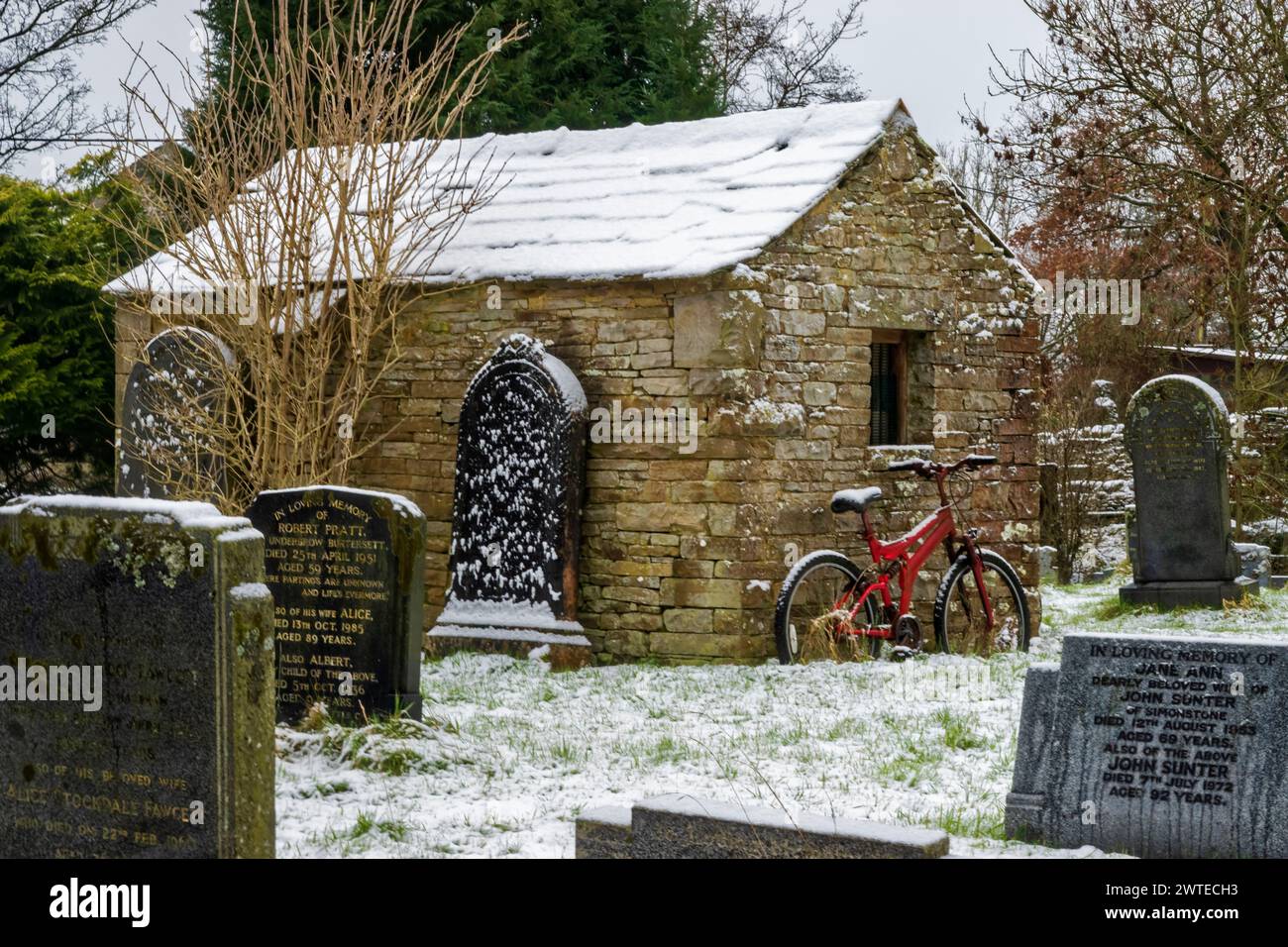 Hardraw Friedhof an einem verschneiten Morgen. Ein rotes Fahrrad beugt sich gegen den Steinschuppen. Stockfoto