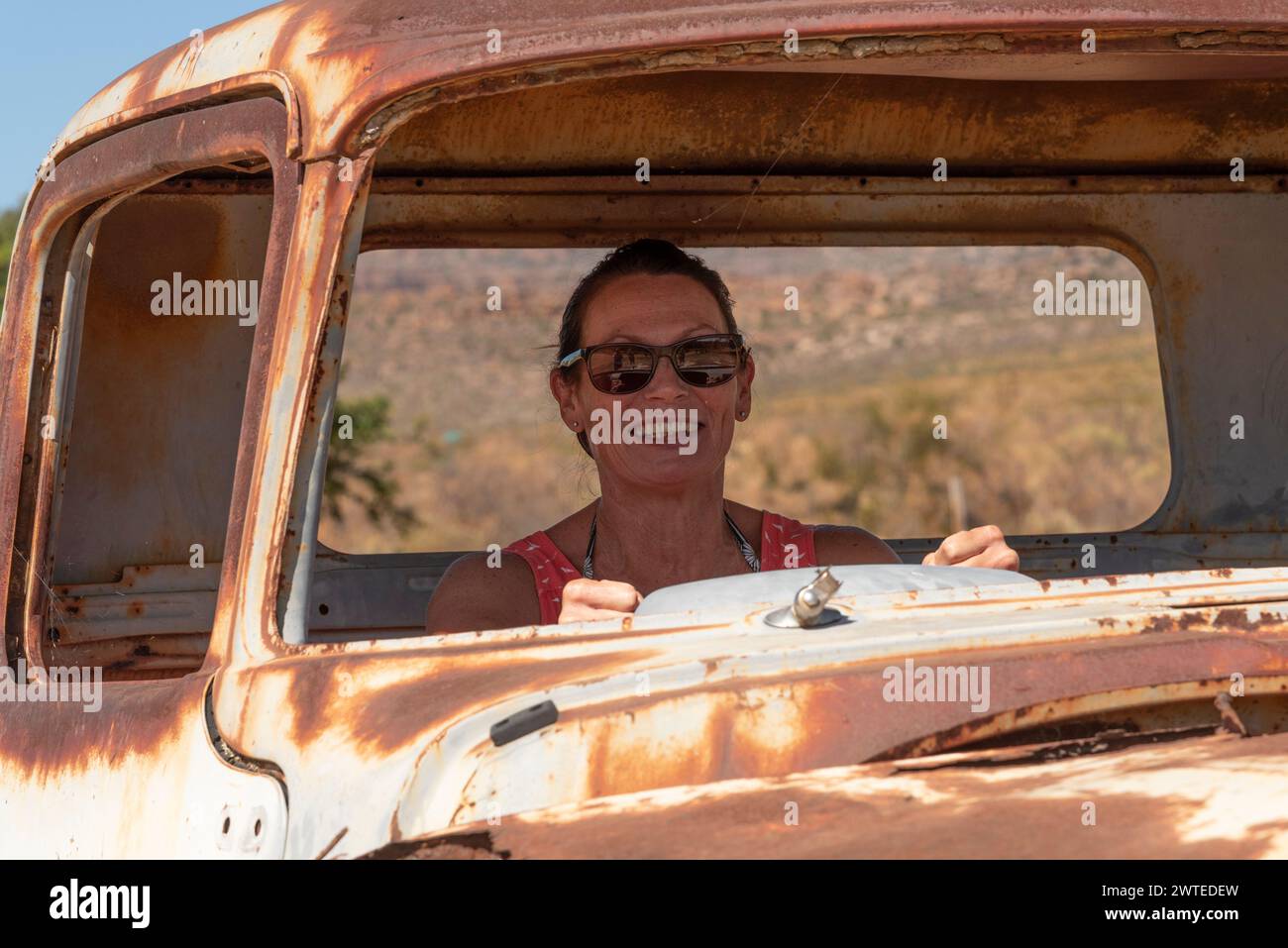 Südafrika. 16/02/2024. Attraktive Frau posiert mit einem alten rostigen amerikanischen Auto am Straßenrand in der Swartland-Region Südafrikas. Stockfoto