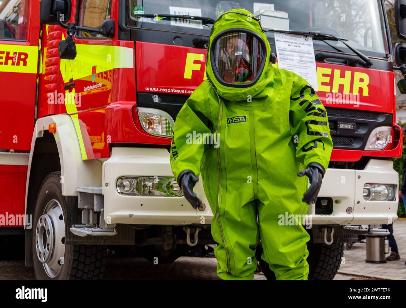 Schwabmünchen, Bayern, Deutschland - 17. März 2024: Feuerwehr mit Schutzausrüstung und grünem Chemikalienschutzanzug CSA, für Gefahrguteinsätze vor einem Feuerwehrfahrzeug oder Feuerwehrfahrzeug. Beim Frühlingsfest in Schwabmünchen, Bayern *** Feuerwehrmann mit Schutzausrüstung und grünem Chemikalienschutzanzug CSA, für Gefahrguteinsätze vor einem Feuerwehrauto, bzw. Einsatzfahrzeug der Feuerwehr. Auf dem Frühlingsfest Schwabmünchen, Bayern Stockfoto