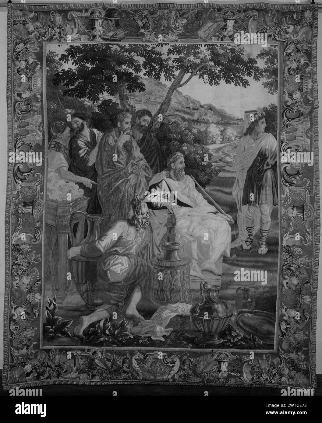 Telemachus-Szene. Unbekannt ca. 1700 Gobelin Abmessungen: H 94 x B 79 cm Gobelin Materialien/Techniken: Unbekannt Kultur: Französisches Weberzentrum: Beauvais Besitz Geschichte: Französisch & Co. Im Landschaftsbild thronender Mann mit Zepter, 4 männliche Figuren hinter dem Thron und 1 männliche Figur auf R des Throns; alle blicken in Richtung R; Platte und Gefäße auf dem Boden vor dem Thron (UPR BRD) Kopf mit strahlenden Flammen (=Sonne) in Kartusche, flankiert von Eulen, offenen Büchern und Gefäßen; (LWR BRD) Kopf mit am Hals befestigten Flügeln in Kartusche, flankiert von Kriegstrophäen und Gefäßen; (L & R BRD) Kartusche flankiert von Girlande Stockfoto