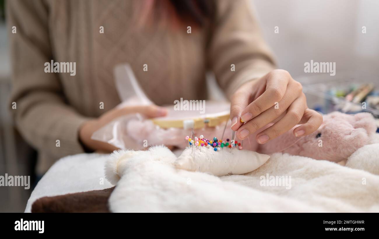Ein Nahbild einer Frau, die eine Nadel an ein Nadelkissen klebt, ein Tuch näht, zu Hause handgemachte Gegenstände bastelt. Handarbeit-Konzept Stockfoto