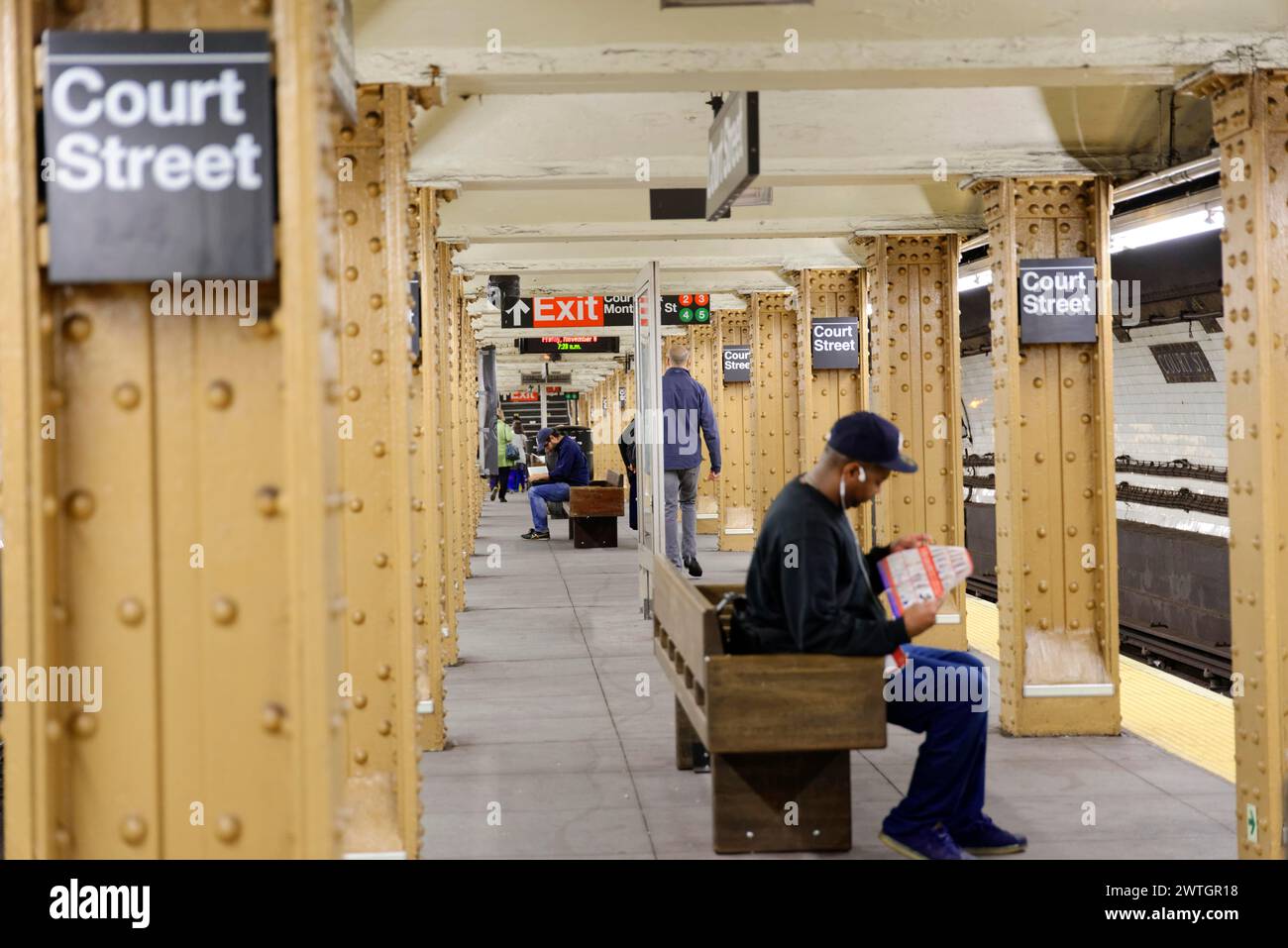 Menschen, die in einer unterirdischen Station mit gelben Säulen und Schildern sitzen und stehen, Manhattan, New York City, New York, USA, Nordamerika Stockfoto