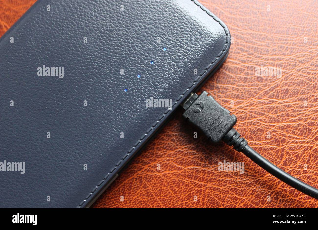 Blaue Diodenanzeigen der Ladewaage, die den Ladezustand der Powerbank auf Lederoberfläche anzeigen Stockfoto