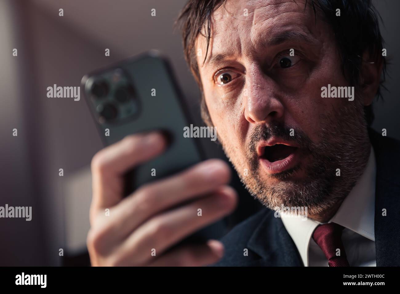 Schockierter Geschäftsmann, der Textnachrichten auf dem Smartphone liest, mit überraschtem Gesichtsausdruck und selektivem Fokus Stockfoto