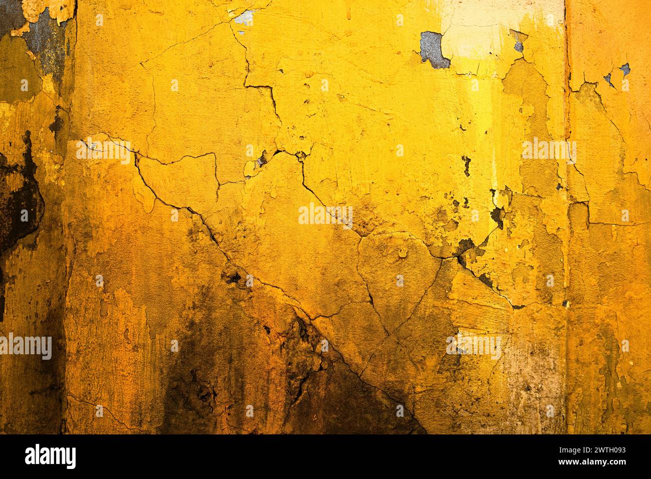 Leuchtend gelbe Wand eines alten Ruinenhauses mit Rissen und Flecken als Hintergrund und Textur Stockfoto