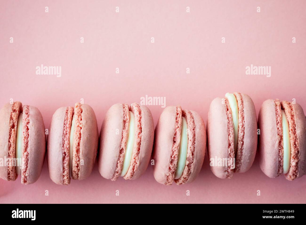 Eine ordentliche Reihe von pastellrosa Macarons auf einem roten Hintergrund Stockfoto