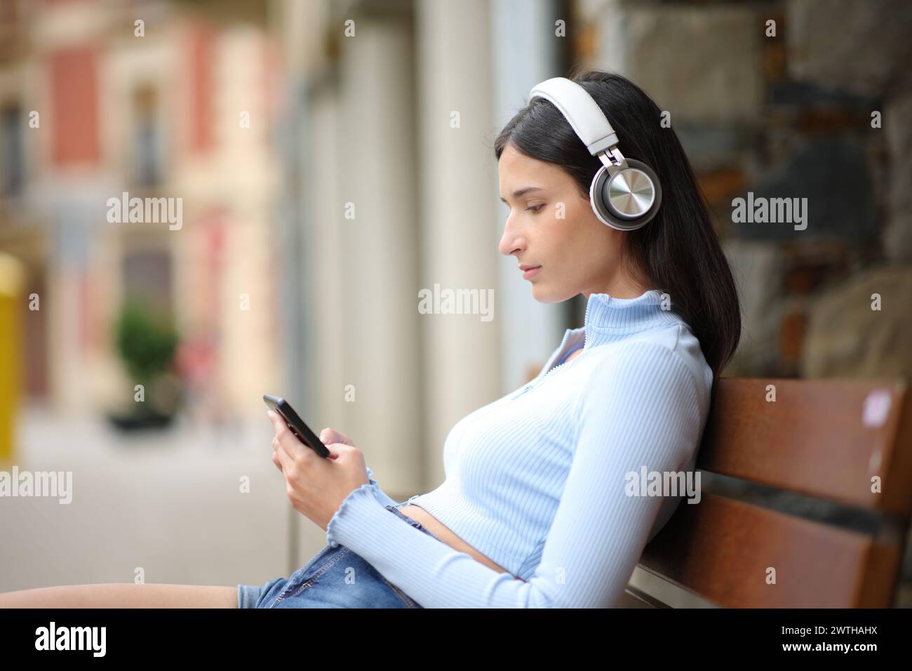 Profil einer entspannten Frau, die Telefon und Kopfhörer auf der Straße benutzt Stockfoto