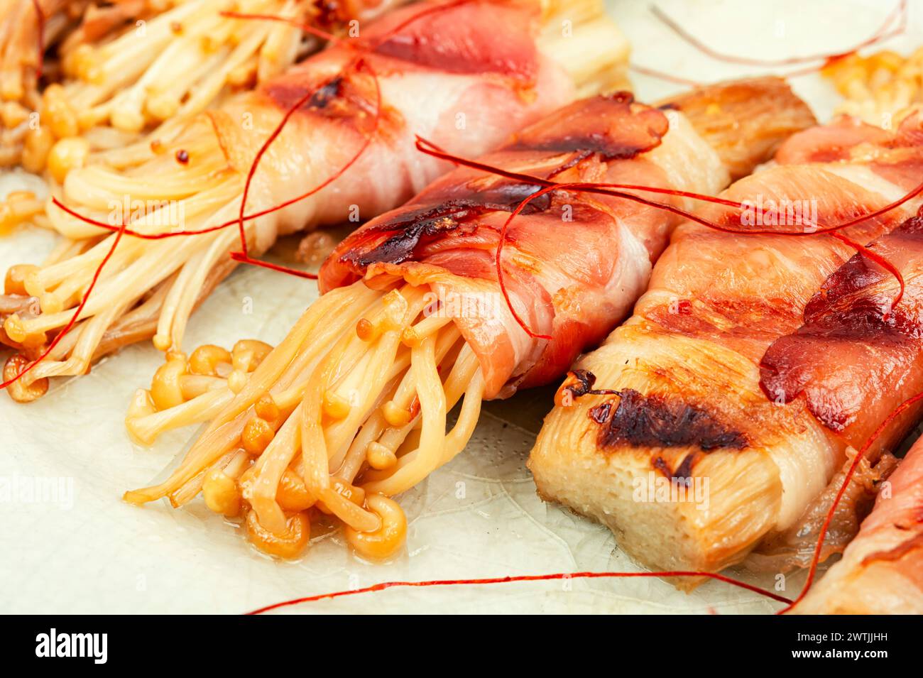 Enoki- oder Eokitake-Pilz in Speck auf Teller geröstet. Mit Speck gewickelter Pilz, Rolle. Stockfoto