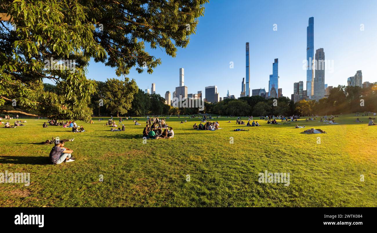 New York City, Central Park Sheep Meadow am Spätsommernachmittag, wo sich die Leute auf dem Gras in der Sonne entspannen. Blick auf die Wolkenkratzer der Billionaires' Row Stockfoto