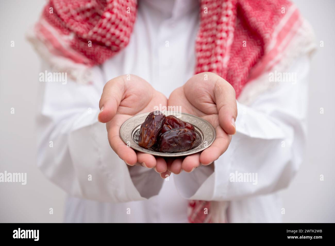 arabische Mann hält Dates repräsentiert Gastfreundschaft und Großzügigkeit, die Kandura mit Keffiyeh auf isoliertem weißen Hintergrund für eid-Feiern tragen Stockfoto