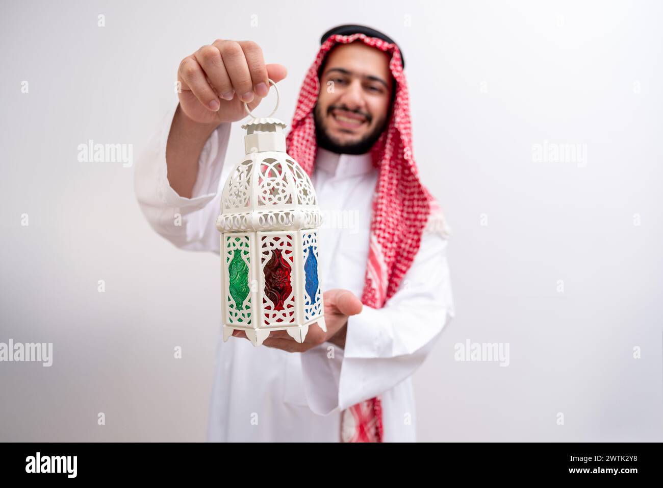 Ein arabischer Mann trägt die würdevolle Kleidung von Kandoura und Keffiyeh und erweitert ein Symbol der Gastfreundschaft und Großzügigkeit, indem er Fanous hält. Gegen eine bac Stockfoto