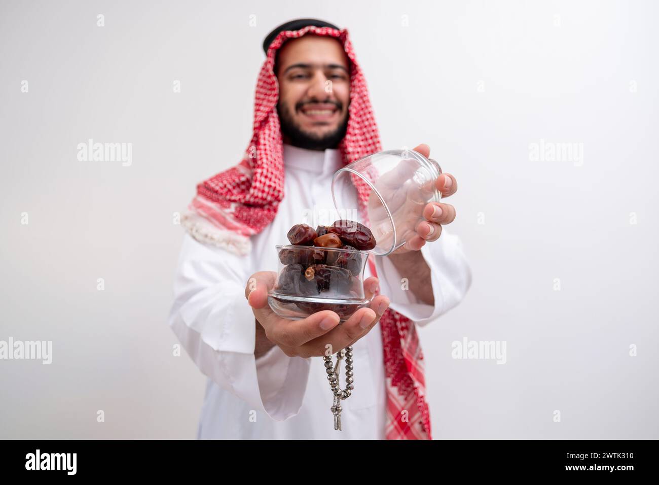 arabische Mann hält Dates repräsentiert Gastfreundschaft und Großzügigkeit, die Kandura mit Keffiyeh auf isoliertem weißen Hintergrund für eid-Feiern tragen Stockfoto