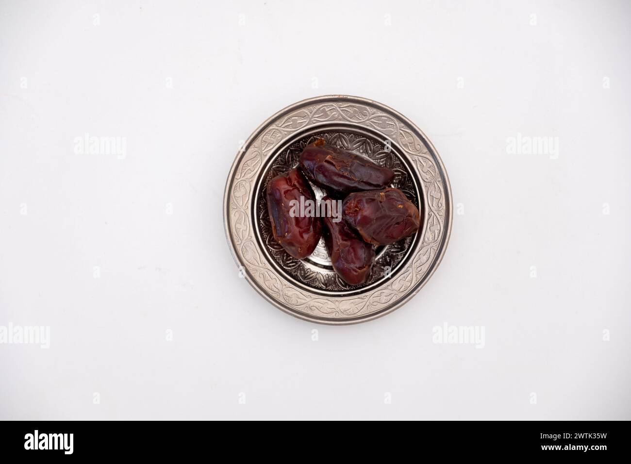 Eine wunderschön geschnitzte Blechschale, die mit komplizierten islamischen Dekorationen verziert ist, überflutet mit üppigen Datteln und Symbolen Stockfoto