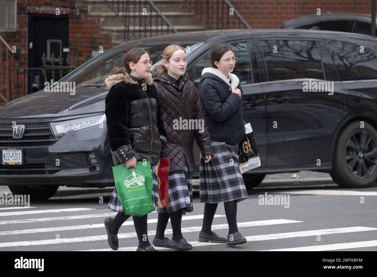 Orthodoxe jüdische Klassenkameraden, die dieselben Schottenröcke tragen, überqueren eine Straße in Brooklyn, New York. Stockfoto