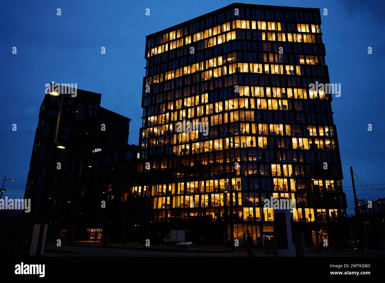 Das Bürogebäude beleuchtet den Abend mit Fenstern, die in der Abenddämmerung leuchten und das städtische Arbeitsleben nach Geschäftsschluss veranschaulichen Stockfoto