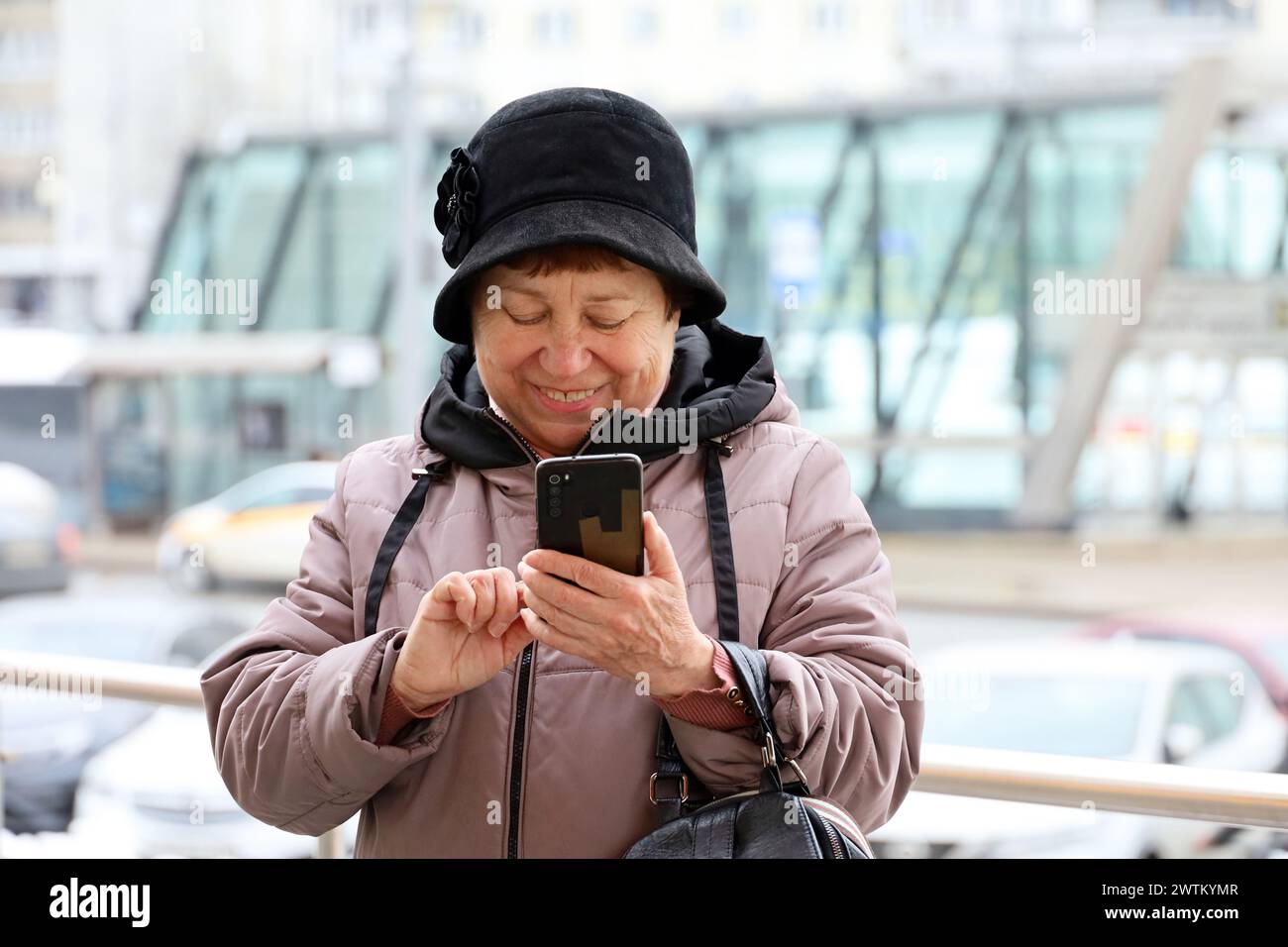 Glückliche alte Frau, die im Frühjahr mit dem Smartphone auf der Stadtstraße läuft Stockfoto