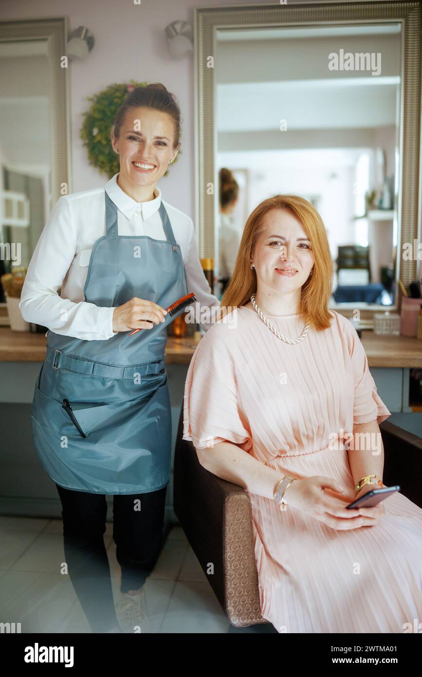Friseurin im modernen Friseurstudio mit Haarbürste und Klientin. Stockfoto