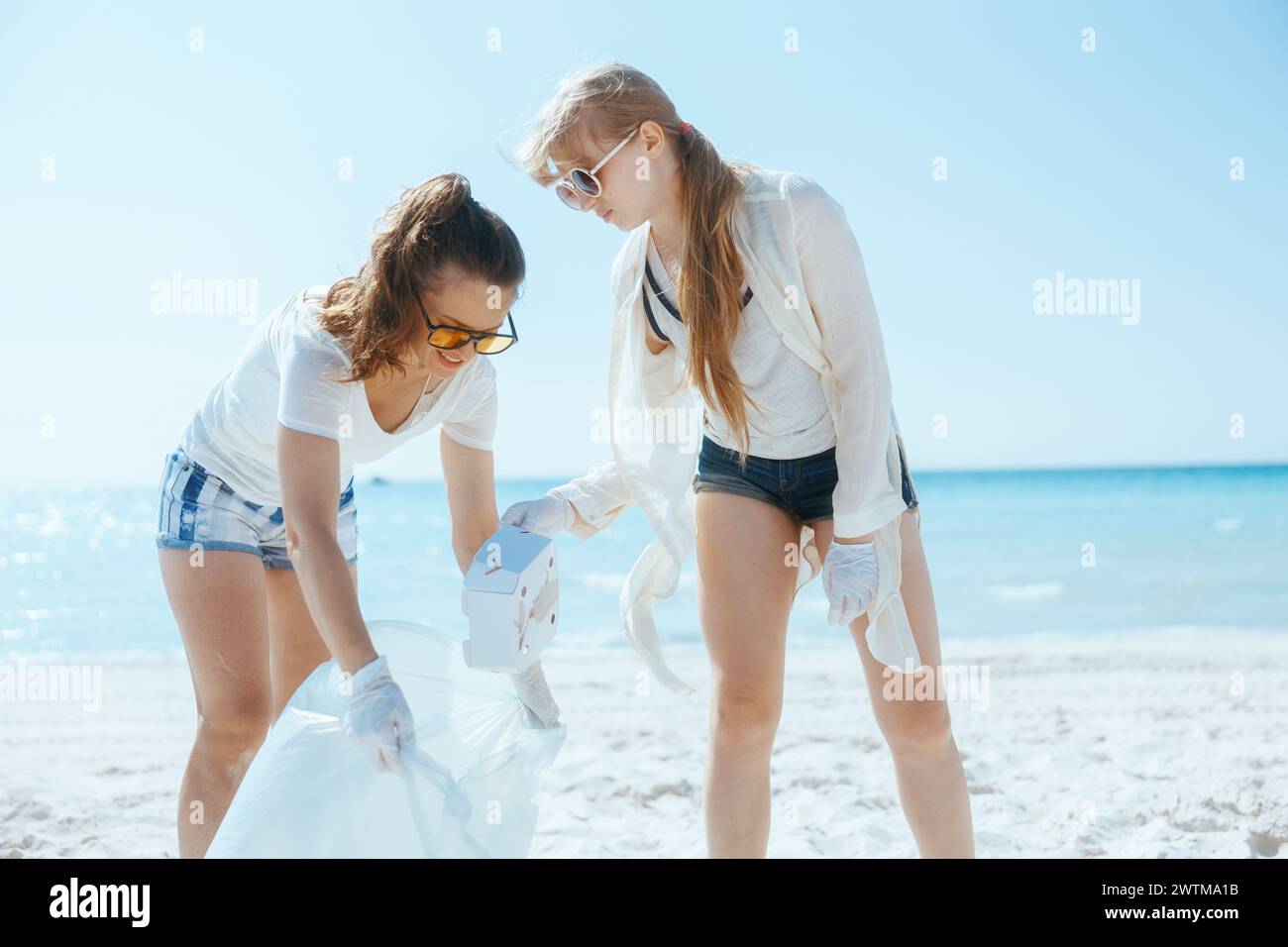 Lächelnde Frauen, die freiwillig am Strand mit Müllsäcken Müll sammeln. Stockfoto