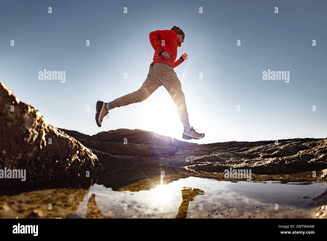 Der Läufer der männlichen Silhouette läuft früh am Morgen über einer Pfütze. Ruhige Szene mit Reflexion im Wasser Stockfoto