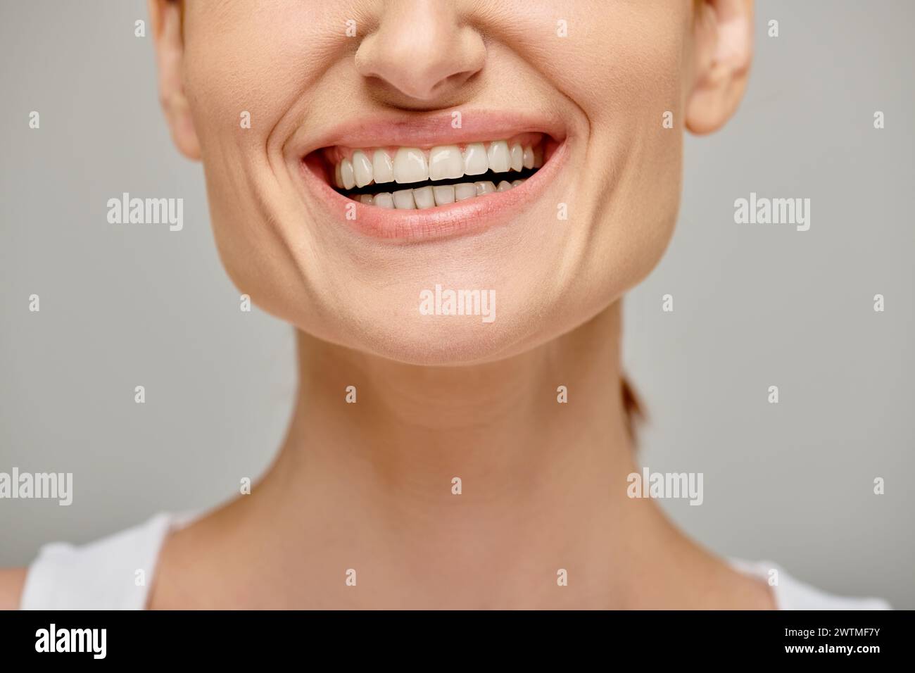 Zugeschnittene Ansicht einer aufgeregten Frau, die ein fröhliches und gesundes Lächeln auf grauem Hintergrund ausstrahlt, weiße Zähne Stockfoto