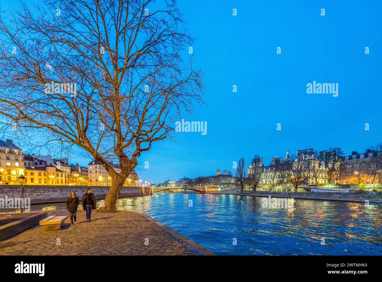 Ein Paar genießt einen Spaziergang in der Dämmerung entlang der seine, während das Ambiente von Paris um sie herum leuchtet. Stockfoto