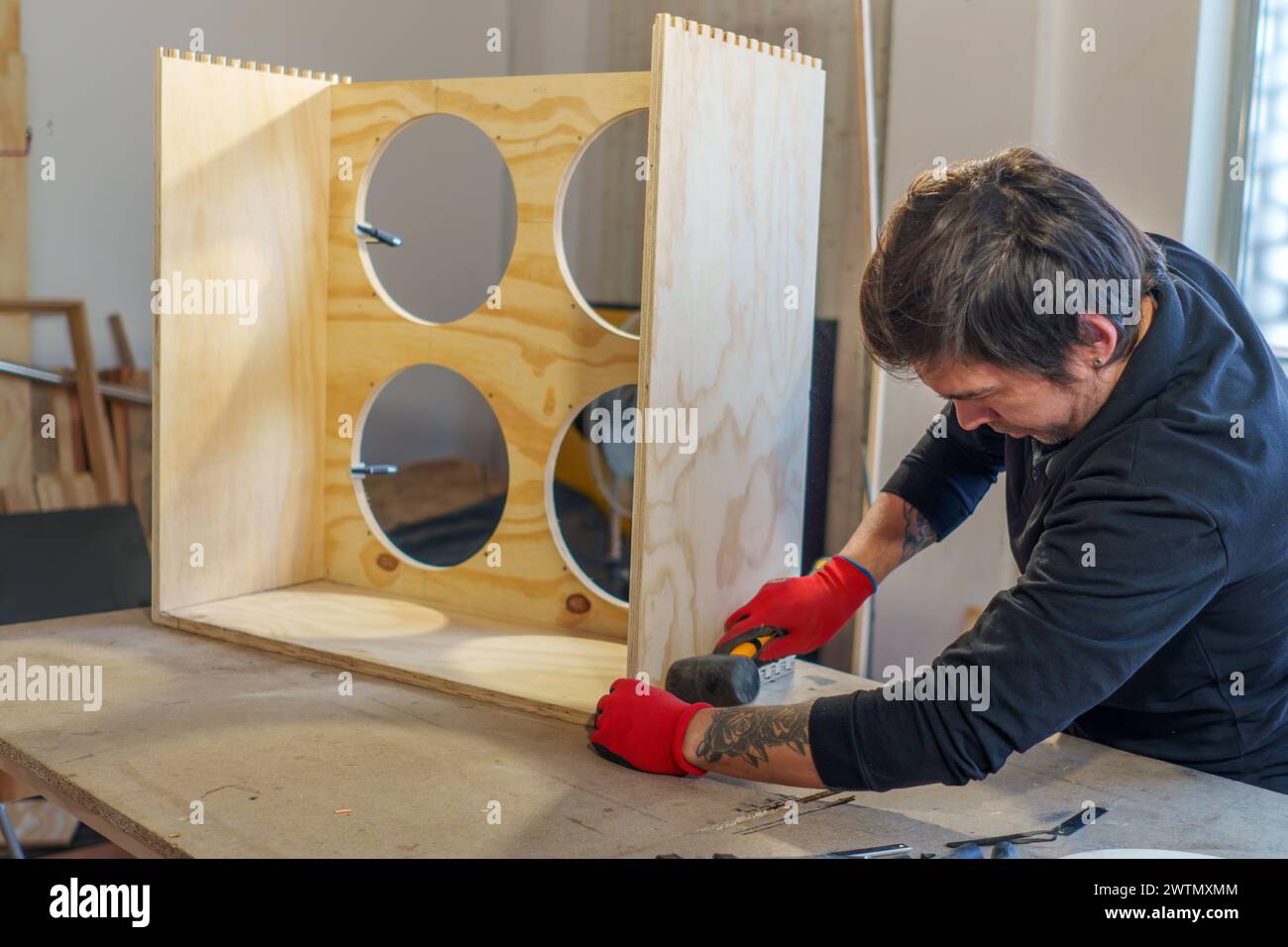 Ein hispanischer Zimmermann mittleren Alters, der in seiner Tischlerei steht und ein Möbelstück zusammenbaut Stockfoto