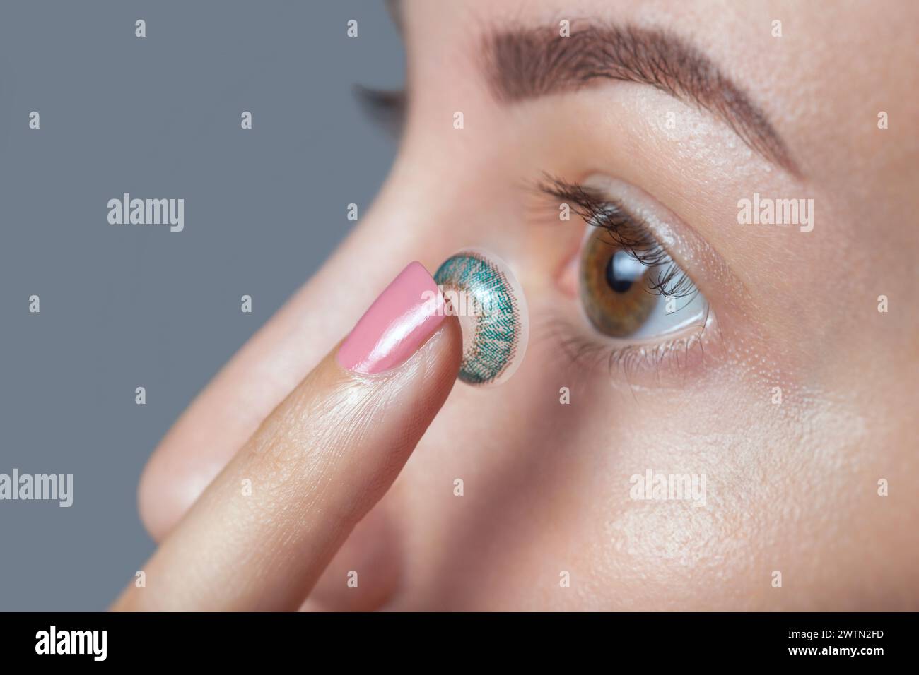 Die Frau hält eine blaue Kontaktlinse am Finger. Augenpflege und die Wahl zwischen den Mitteln zur Verbesserung des Sehens. Stockfoto
