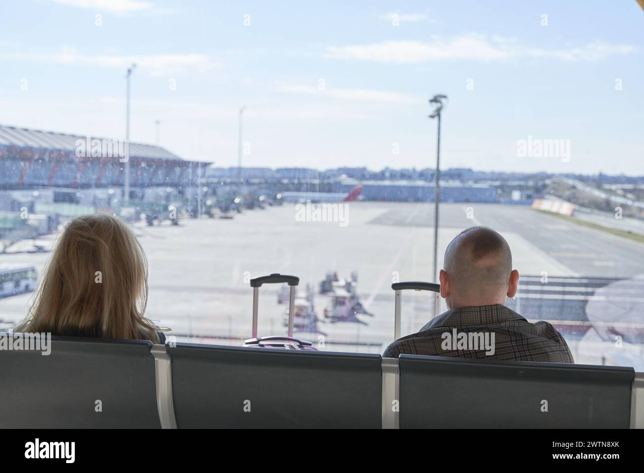 Paare warten am Flughafen in der Nähe des Fensters, nicht erkennbare Paare sitzen, während sie auf ihren Flug warteten Stockfoto