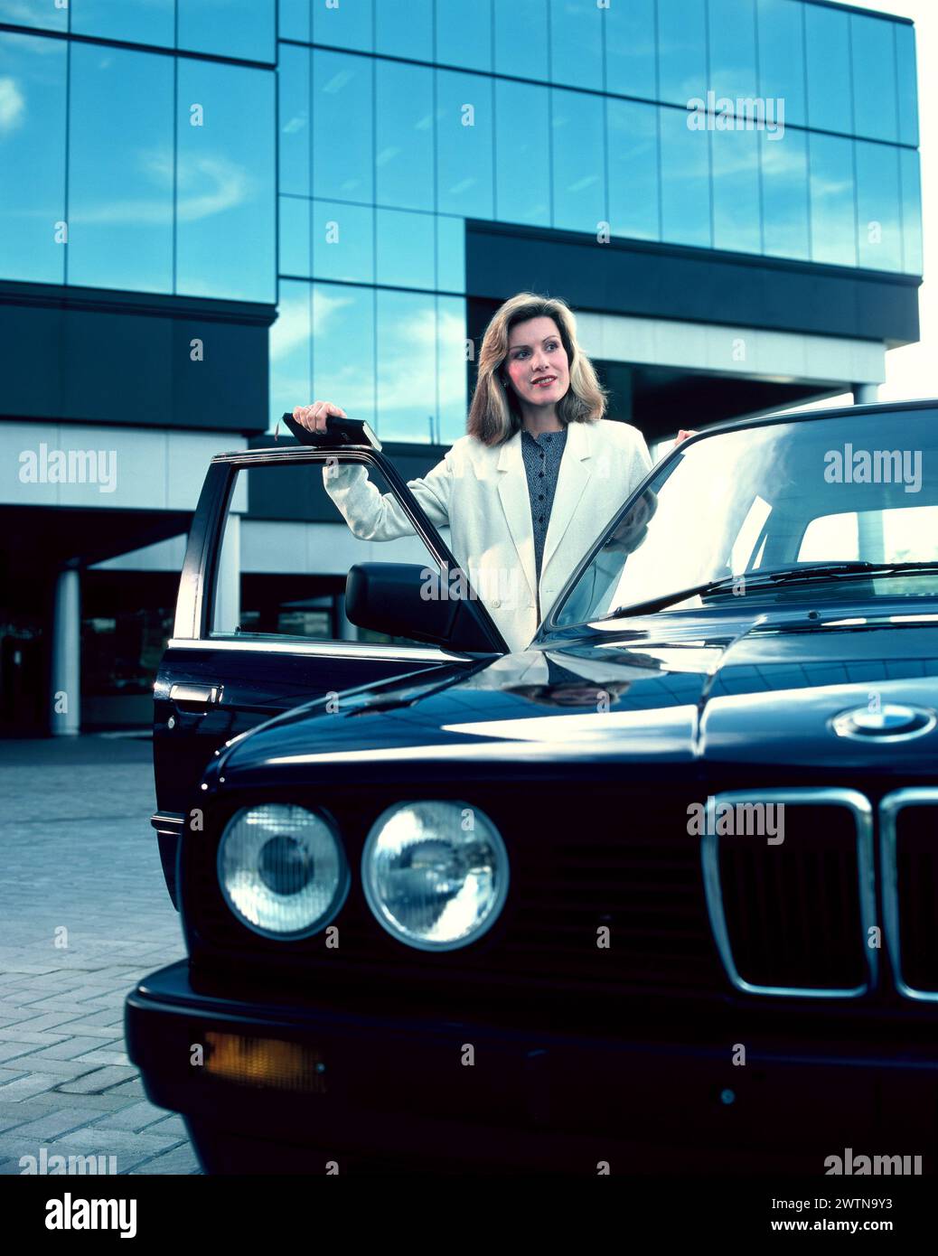 Junge Frau vor dem Bürogebäude bei ihrem Oldtimer-BMW. Stockfoto