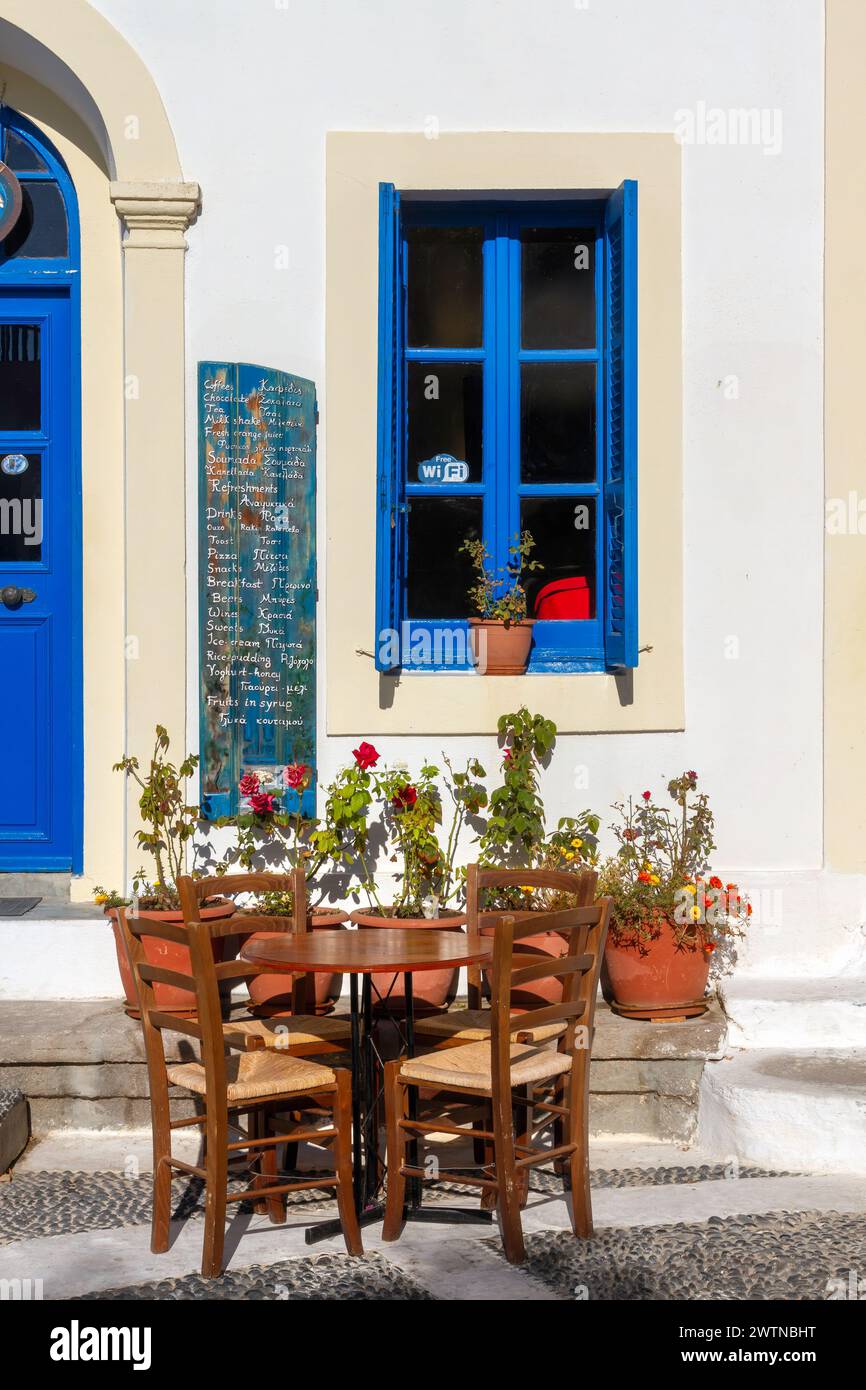 Traditionelles Café (Kafenio) mit Holzstühlen und Preisliste auf einem Holzbrett, im malerischen Dorf Nikia auf der Insel Nisyros, Griechenland. Stockfoto