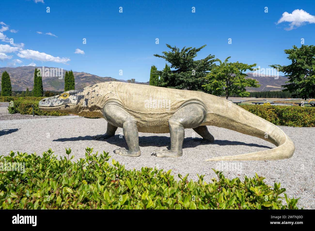 Cromwell, Neuseeland, 3. Januar 2024: Eine beige Dinosaurier-Statue stand mitten im Schritt vor der Landschaft des Highlands Parks, mit Sträuchern im Vordergrund und Stockfoto