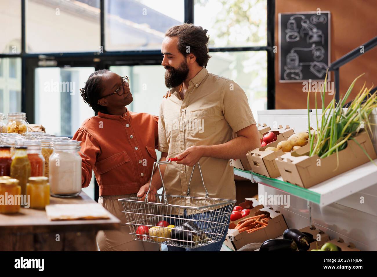 Glückliches multikulturelles Paar, das in einem umweltfreundlichen Laden stöbert. afroamerikanische Frau und kaukasischer Mann mit einem Korb auf der Suche nach Bio-Lebensmitteln für einen gesunden Lebensstil. Stockfoto