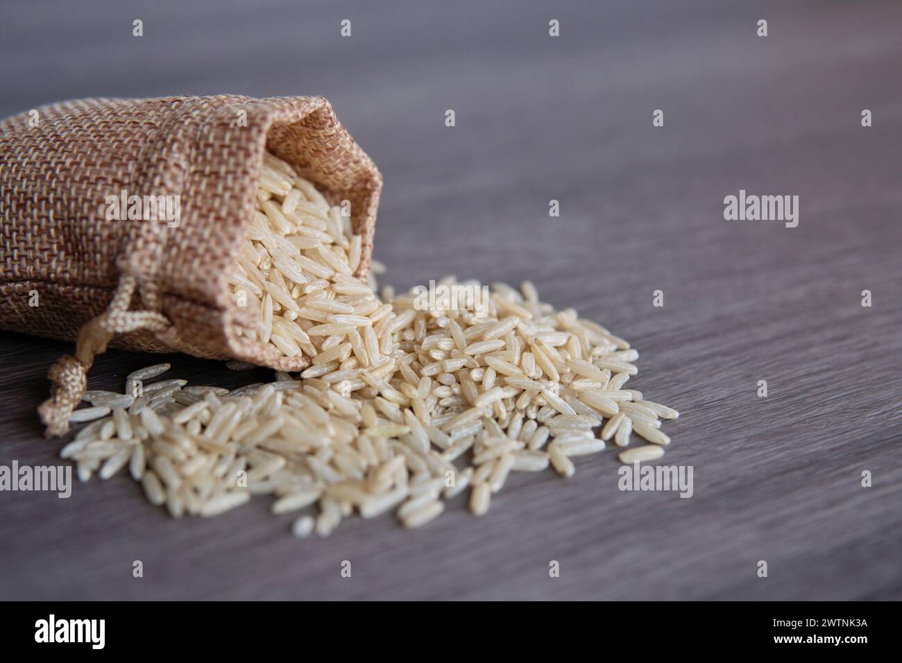 Nahaufnahme von braunem Reis in einem kleinen Sacksack auf Holztisch mit Kopierraum. Stockfoto