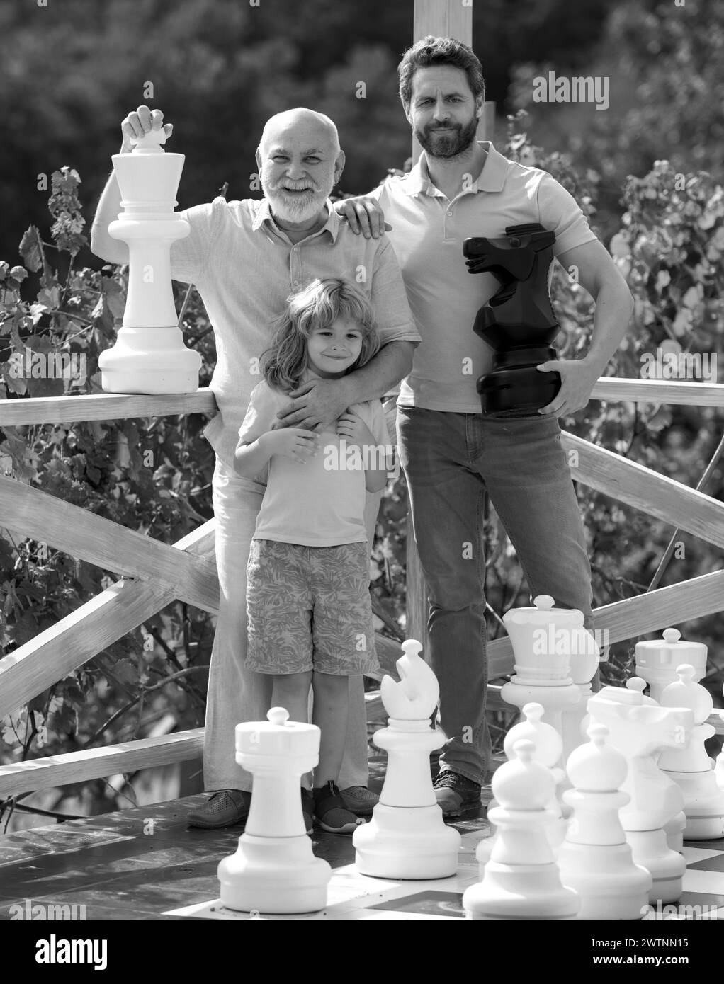 Großvater mit Sohn und Enkel spielen Schach. Erstaunte Männer in verschiedenen Altersgruppen spielen Schachbrett Spiel. Drei-Mann-Generation. Väter Tag Konzept. Stockfoto