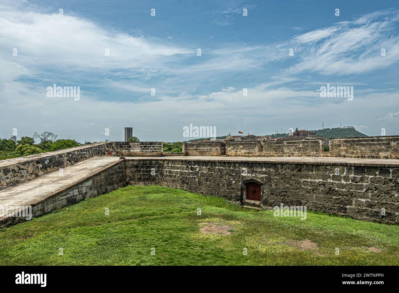 Cartagena, Kolumbien - 25. Juli 2023: Die schwarzbraune Steinmauer Baluarte de Santa Barbara auf der Ostseite der Altstadt unter blauer Wolkenlandschaft. Grünrasen Stockfoto