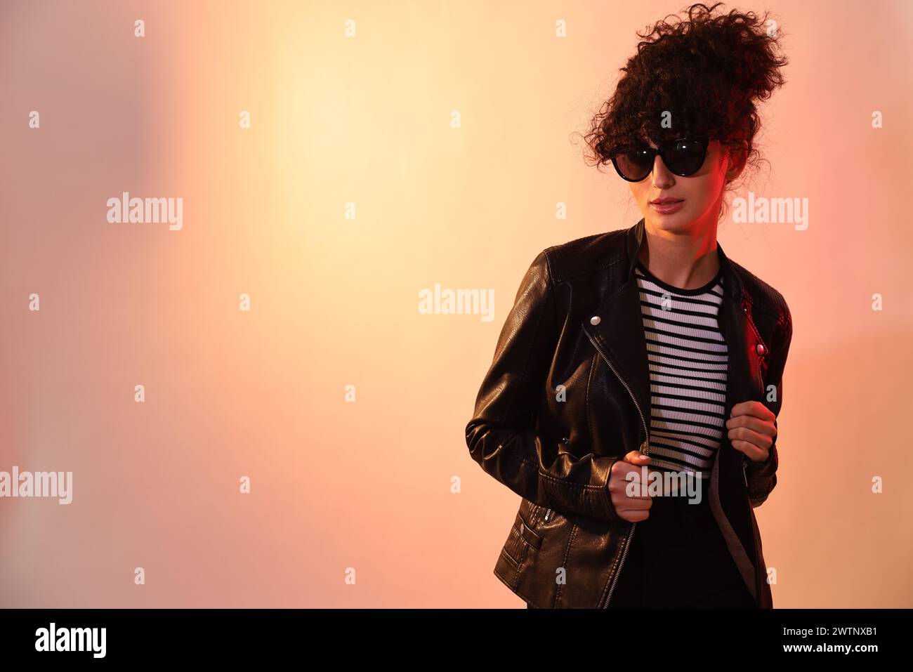 Schöne junge Frau in schwarzer Lederjacke und Sonnenbrille, die auf farbigem Hintergrund in Neonlichtern posiert. Leerzeichen für Text Stockfoto