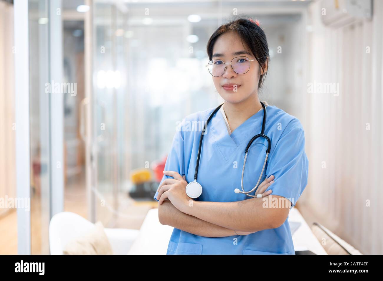 Eine professionelle und selbstbewusste asiatische Ärztin in Peelings, die mit überkreuzten Armen im Krankenhausflur steht. Medizin- und Gesundheitskonzepte Stockfoto