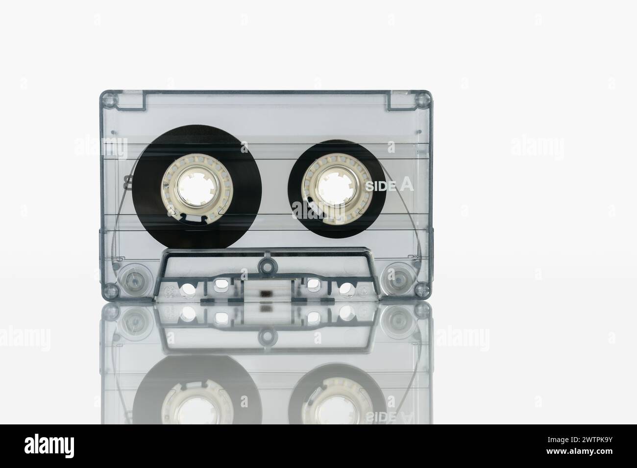 Eine Audiokassette in einer transparenten Hülle steht auf weißem Hintergrund mit Reflexion Stockfoto