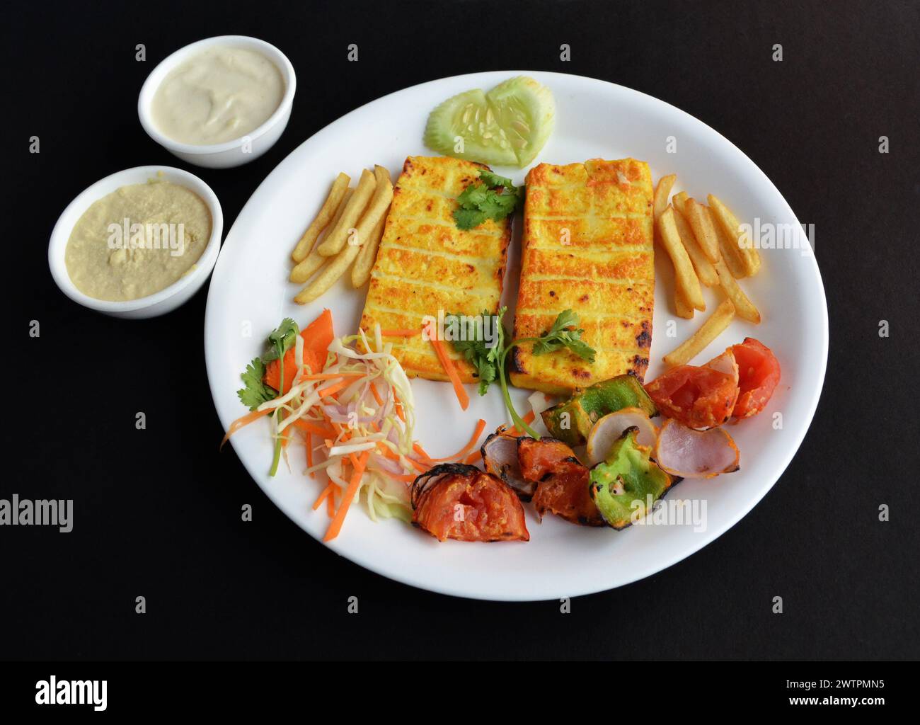 Gegrillter Paneer wird hergestellt, indem der Hüttenkäse in einer kräftigen Masala-Paste mariniert wird. Serviert auf einem weißen Teller mit Salat und Pommes frites. Stockfoto