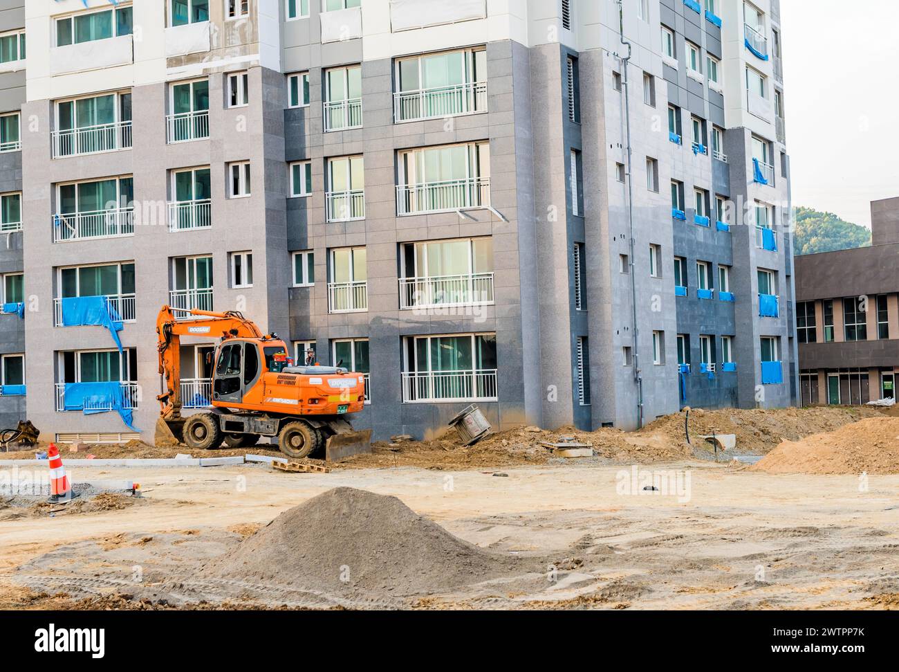 Der Bagger arbeitet in einer Bauzone vor dem Hintergrund eines unvollendeten Wohnkomplexes in Daejeon, Südkorea Stockfoto